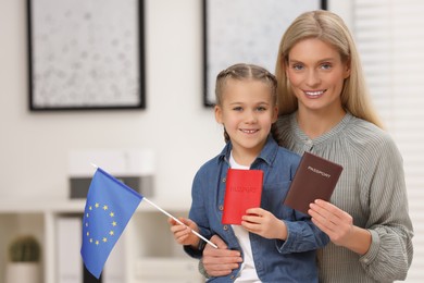 Immigration. Happy woman with her daughter holding passports and flag of European Union indoors