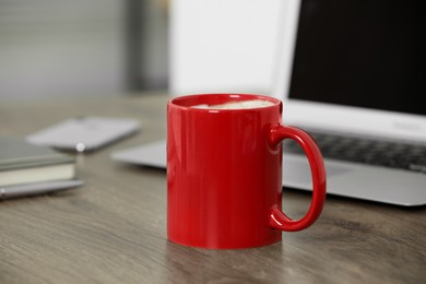 Red ceramic mug with hot drink on wooden table desk at workplace. Mockup for design