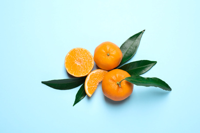 Flat lay composition with fresh ripe tangerines and leaves on light blue background. Citrus fruit