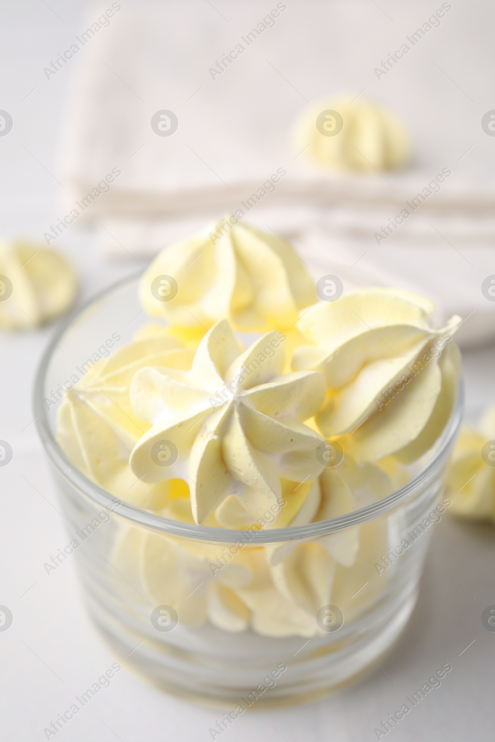 Photo of Tasty meringue cookies in glass on white tiled table