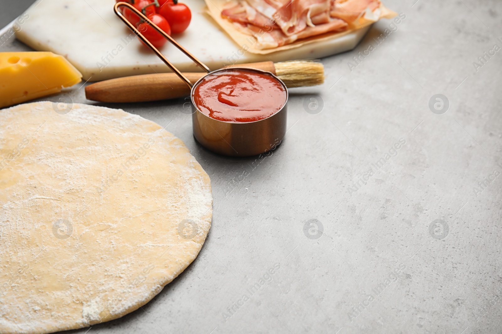 Photo of Raw dough, sauce and cheese on grey table, space for text. Pizza recipe