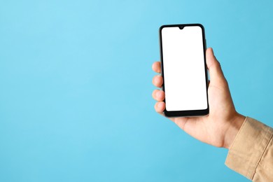 Photo of Man holding smartphone with blank screen on light blue background, closeup. Mockup for design