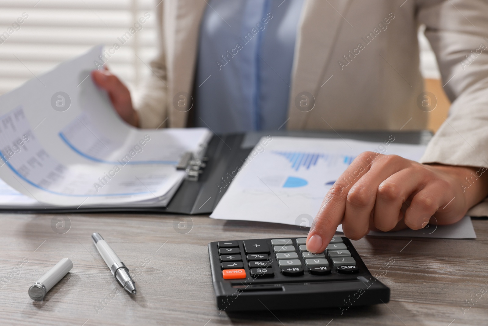 Photo of Woman using calculator at light wooden table in office, closeup