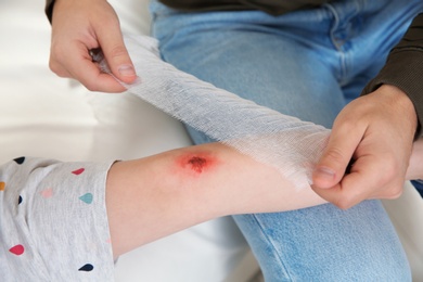 Photo of Father applying bandage on daughter's injured knee at home, closeup. First aid