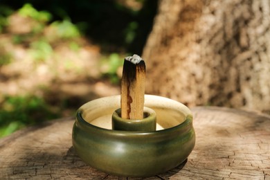 Smoldering palo santo stick in holder on wooden stump outdoors