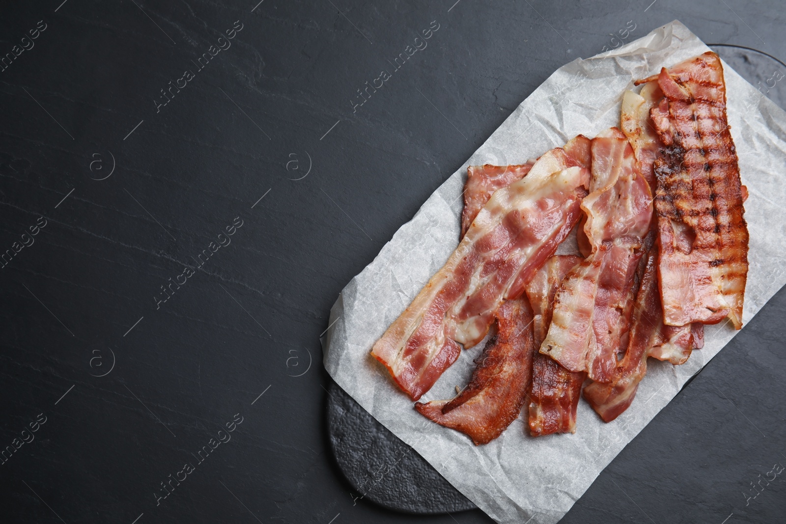 Photo of Slices of tasty fried bacon on dark table, top view. Space for text