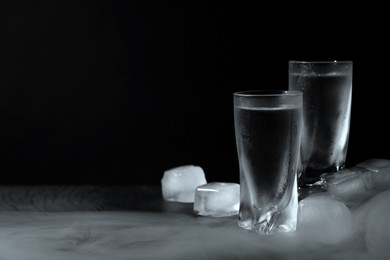 Photo of Vodka in shot glasses with ice on table against black background, space for text