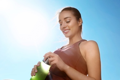 Photo of Young sporty woman holding bottle of water against blue sky on sunny day