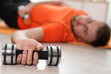 Photo of Lazy young man with sport equipment on floor at home, focus on hand