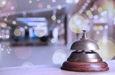 Image of Wooden table with hotel service bell on blurred background. Space for text
