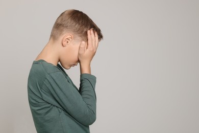 Photo of Boy covering face with hands on light grey background, space for text. Children's bullying