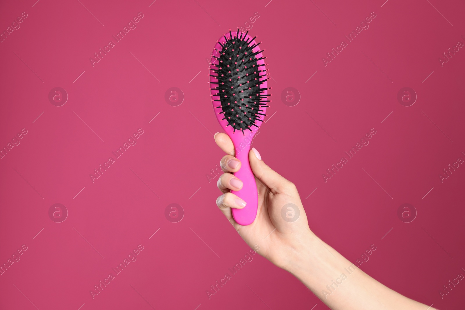 Photo of Woman holding hair brush against crimson background, closeup. Space for text