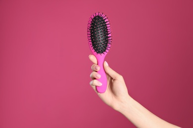 Photo of Woman holding hair brush against crimson background, closeup. Space for text