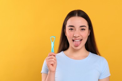 Happy woman with tongue cleaner on yellow background, space for text