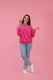 Photo of Smiling young woman taking selfie with smartphone on pink background