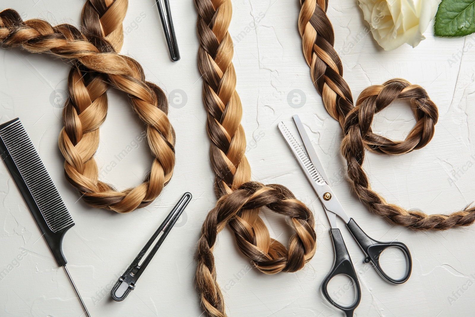 Photo of Flat lay composition with braids and hairdresser's tools on light background