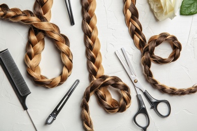 Photo of Flat lay composition with braids and hairdresser's tools on light background