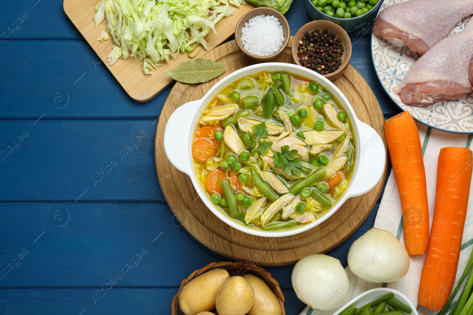 Photo of Saucepan of delicious vegetable soup with chicken and different ingredients on blue wooden table, flat lay. Space for text