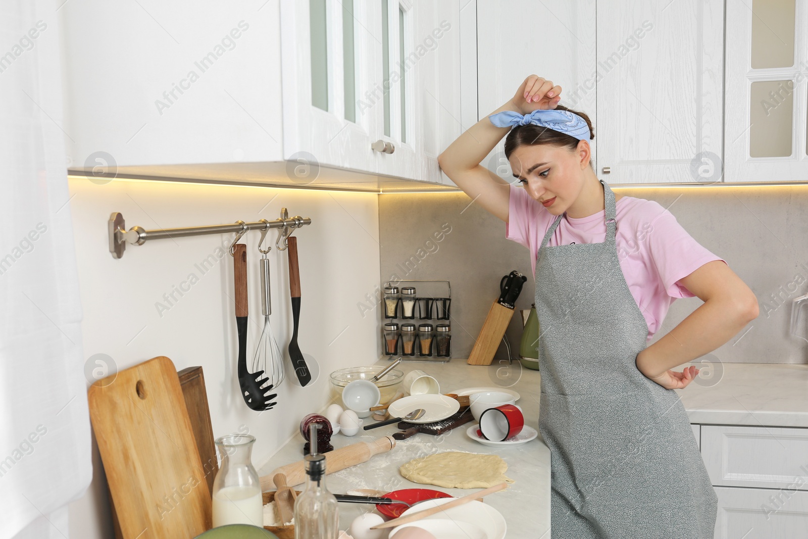 Photo of Tired woman looking at messy countertop with dirty dishware, food and utensils in kitchen