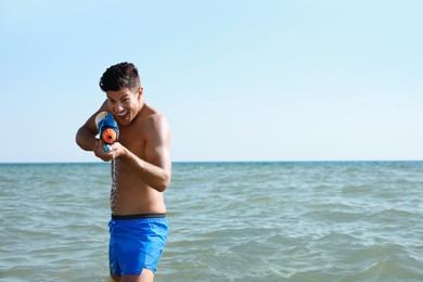 Man with water gun having fun in sea. Space for text