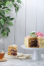 Photo of Delicious cake decorated with macarons and marshmallows and tea served on white marble table, space for text