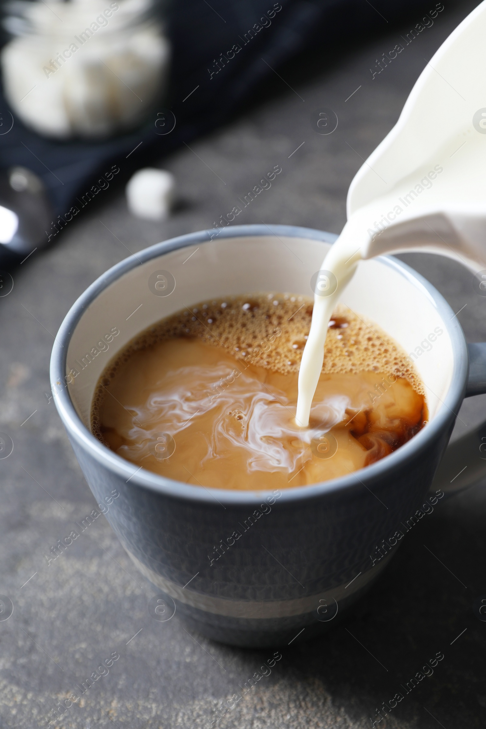 Photo of Pouring milk into cup of coffee on grey table, closeup