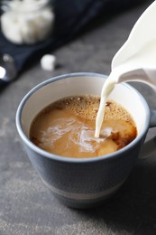 Photo of Pouring milk into cup of coffee on grey table, closeup