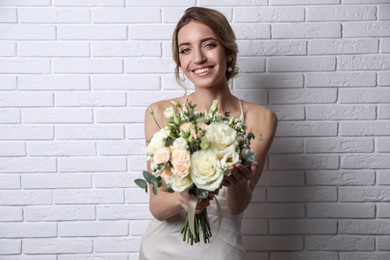 Young bride with beautiful wedding bouquet near white brick wall