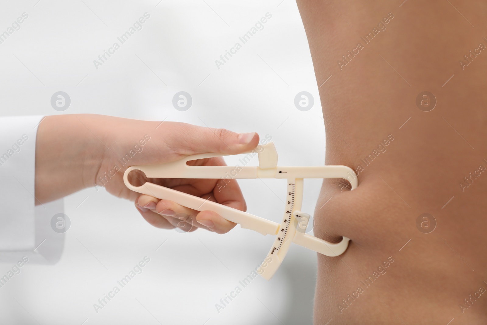 Photo of Nutritionist measuring man's body fat layer with caliper on blurred background, closeup