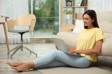 Young woman working with laptop near sofa at home, space for text