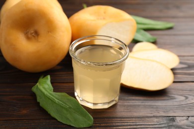 Photo of Glass of fresh natural turnip juice, green leaves, cut and whole roots on wooden table