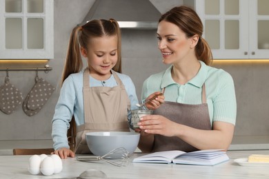 Cute little girl with her mother cooking by recipe book in kitchen