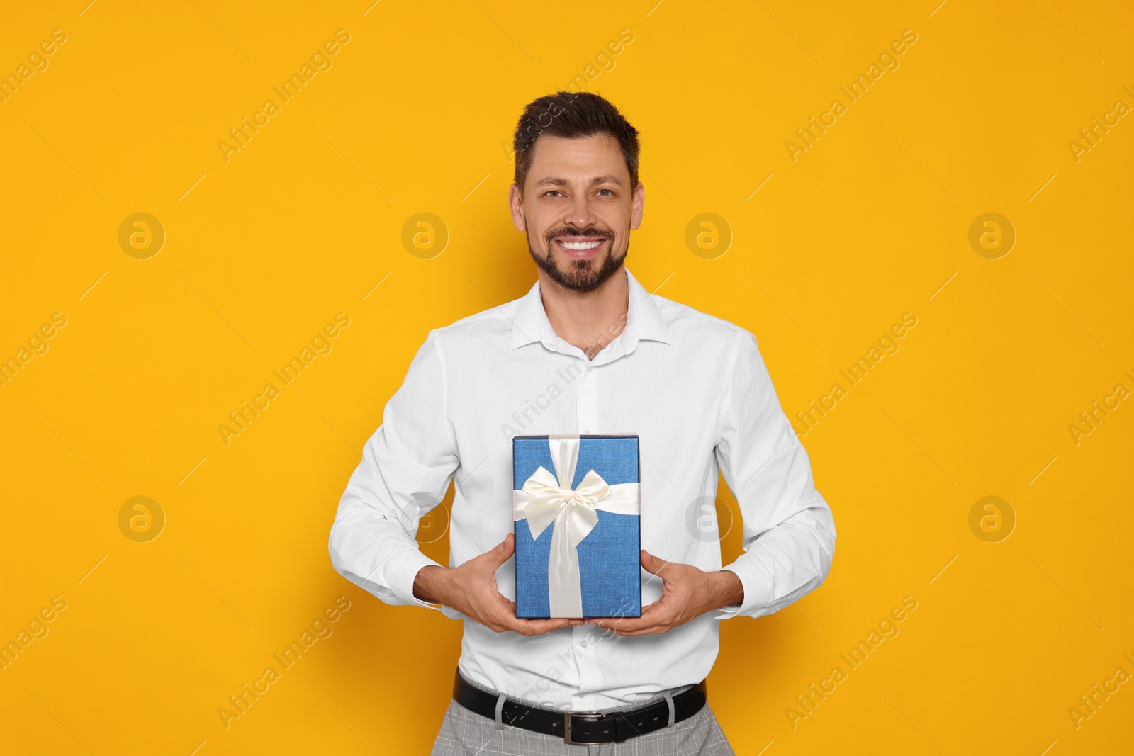 Photo of Happy man with gift box on yellow background