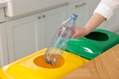 Photo of Garbage sorting. Woman throwing plastic bottle into trash bin indoors, closeup