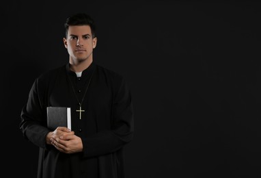 Priest with Bible on black background. Space for text