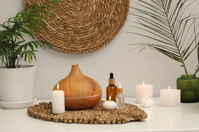 Photo of Spa composition. Essential oil diffuser, cosmetic products, burning candles and plants on table