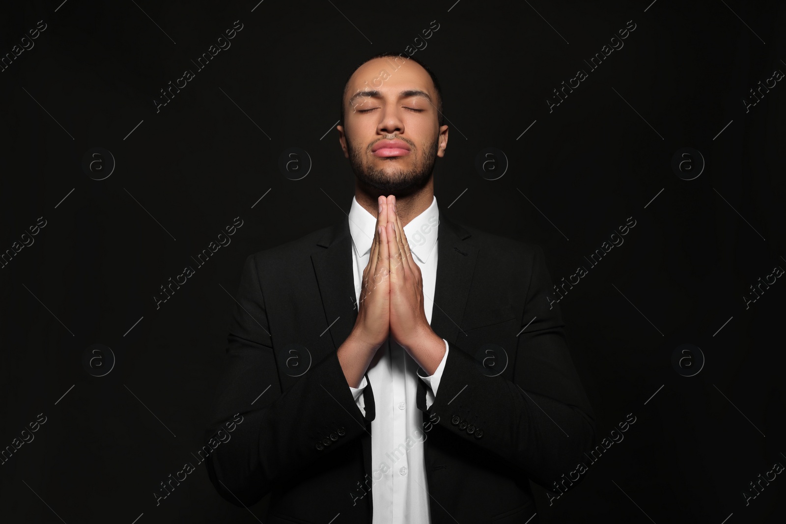 Photo of African American man with clasped hands praying to God on black background