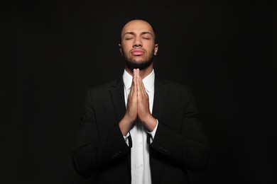 Photo of African American man with clasped hands praying to God on black background