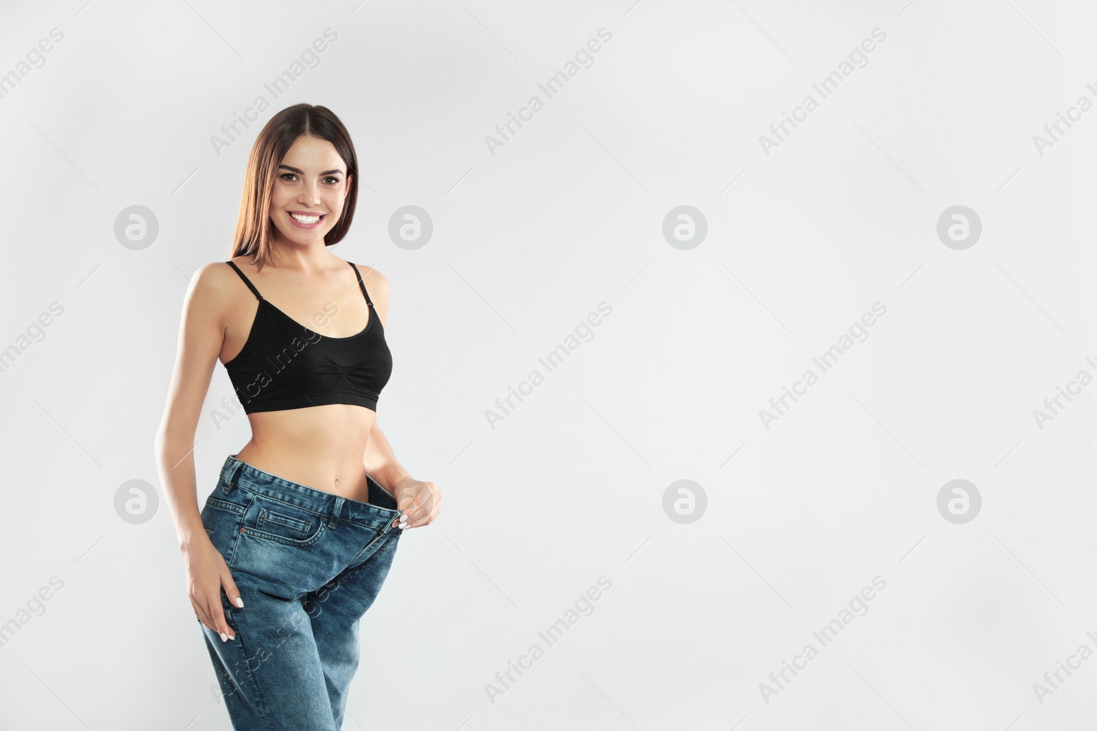 Photo of Attractive young woman with slim body wearing her old big jeans on white background. Space for text