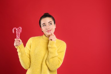 Young woman in yellow sweater holding candy canes on red background, space for text. Celebrating Christmas
