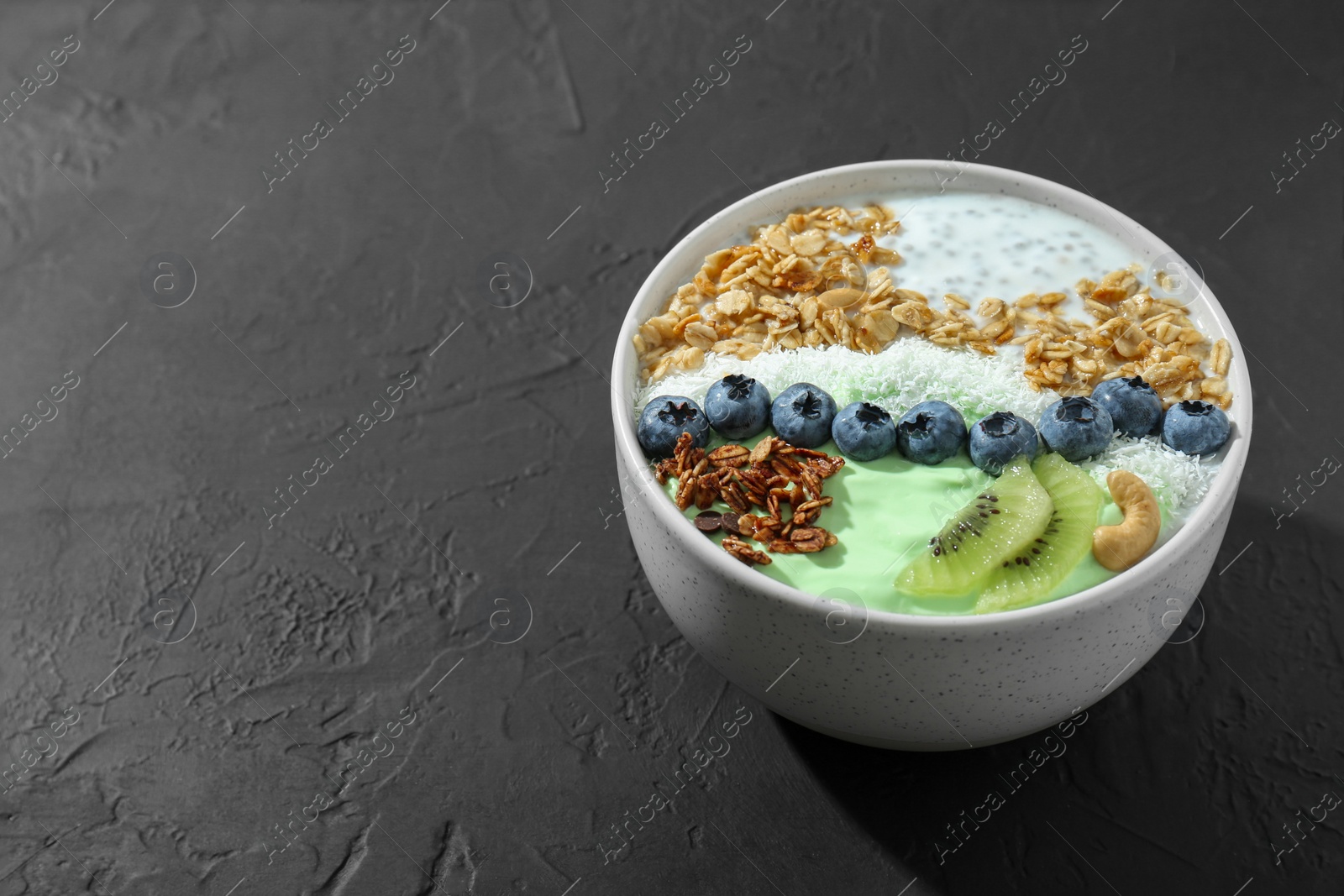 Photo of Tasty smoothie bowl with fresh kiwi fruit, blueberries and oatmeal on black table, space for text