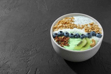 Photo of Tasty smoothie bowl with fresh kiwi fruit, blueberries and oatmeal on black table, space for text