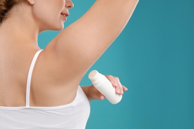 Photo of Young woman applying deodorant to armpit on teal background, closeup