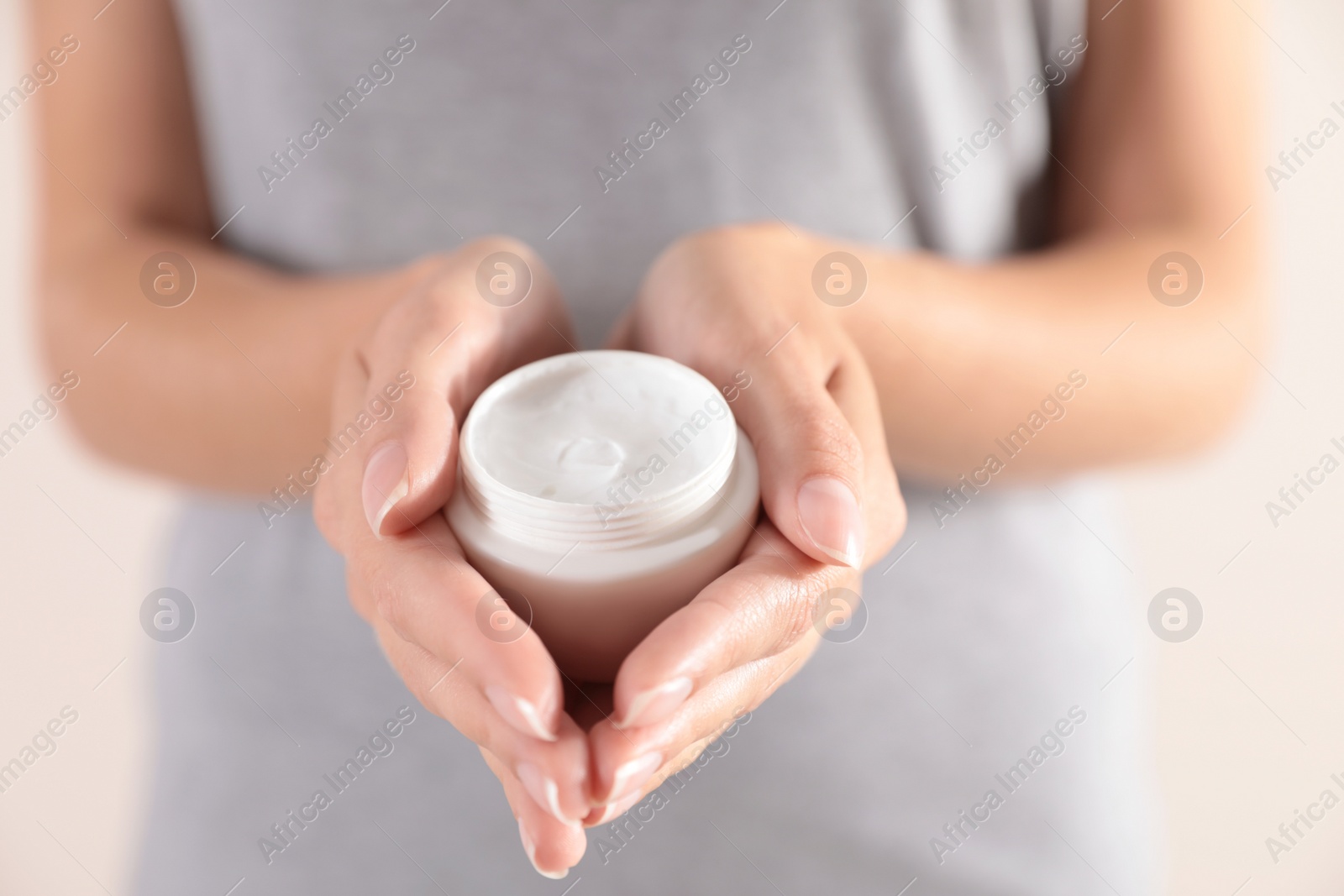 Photo of Young woman holding jar of cream on light background, closeup