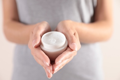 Photo of Young woman holding jar of cream on light background, closeup