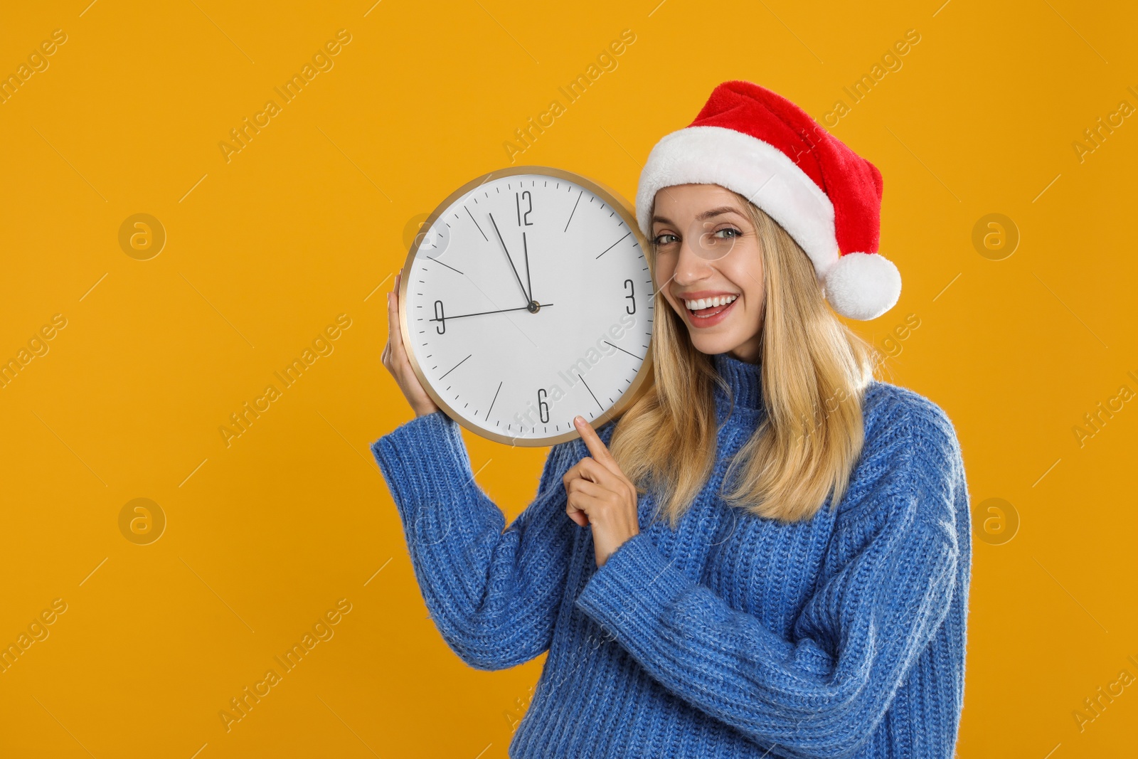 Photo of Woman in Santa hat with clock on yellow background, space for text. New Year countdown