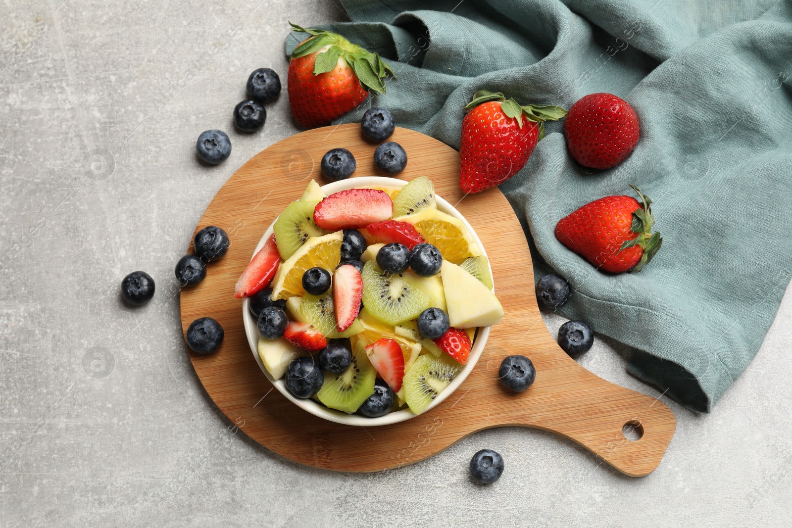 Photo of Tasty fruit salad in bowl and ingredients on gray textured table, flat lay