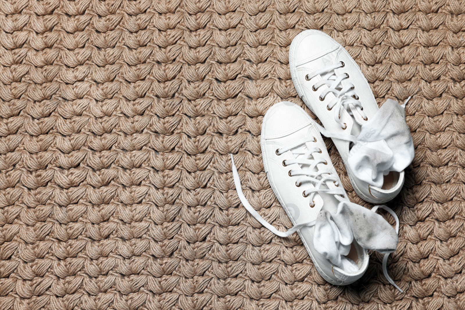 Photo of Sneakers with dirty socks on woven mat indoors, top view. Space for text