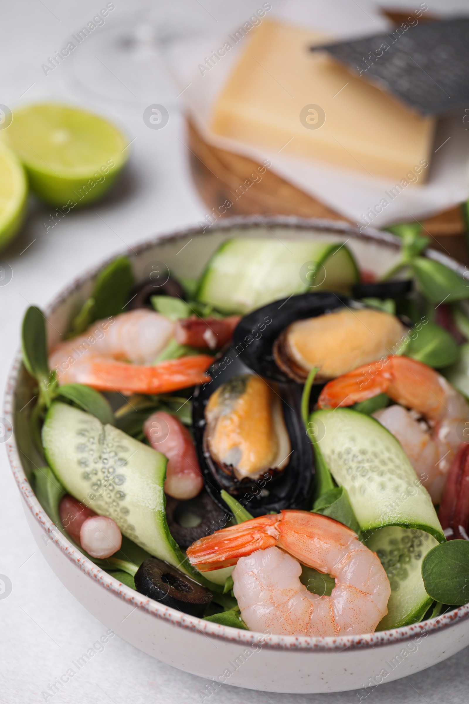 Photo of Bowl of delicious salad with seafood on light grey table, closeup