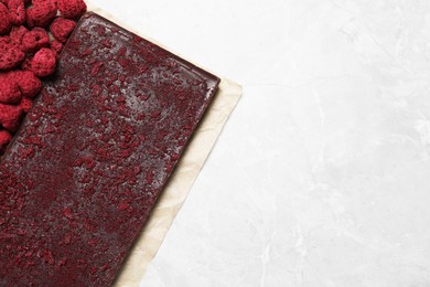 Photo of Chocolate bar with freeze dried raspberries on light marble table, top view. Space for text